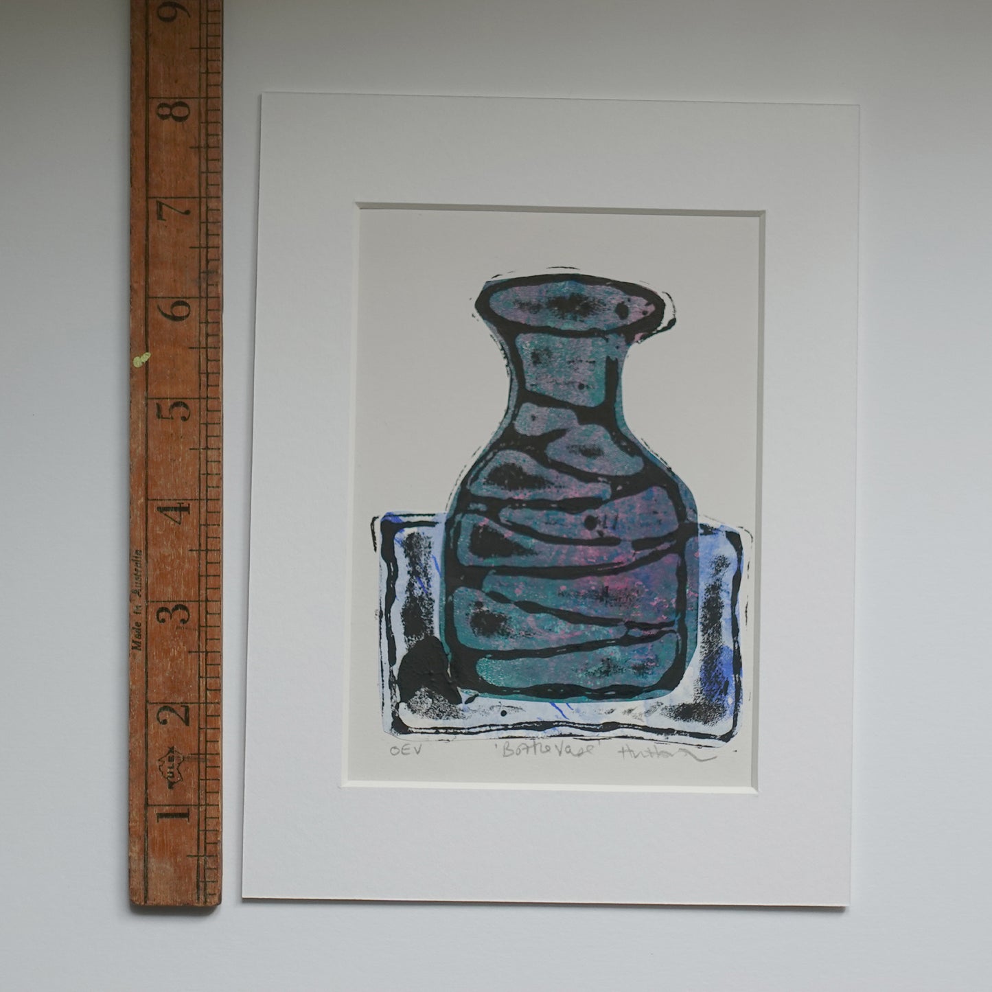 Relief print of bottle vase printed with black ink over chine-collé shown in mount with wooden ruler for scale