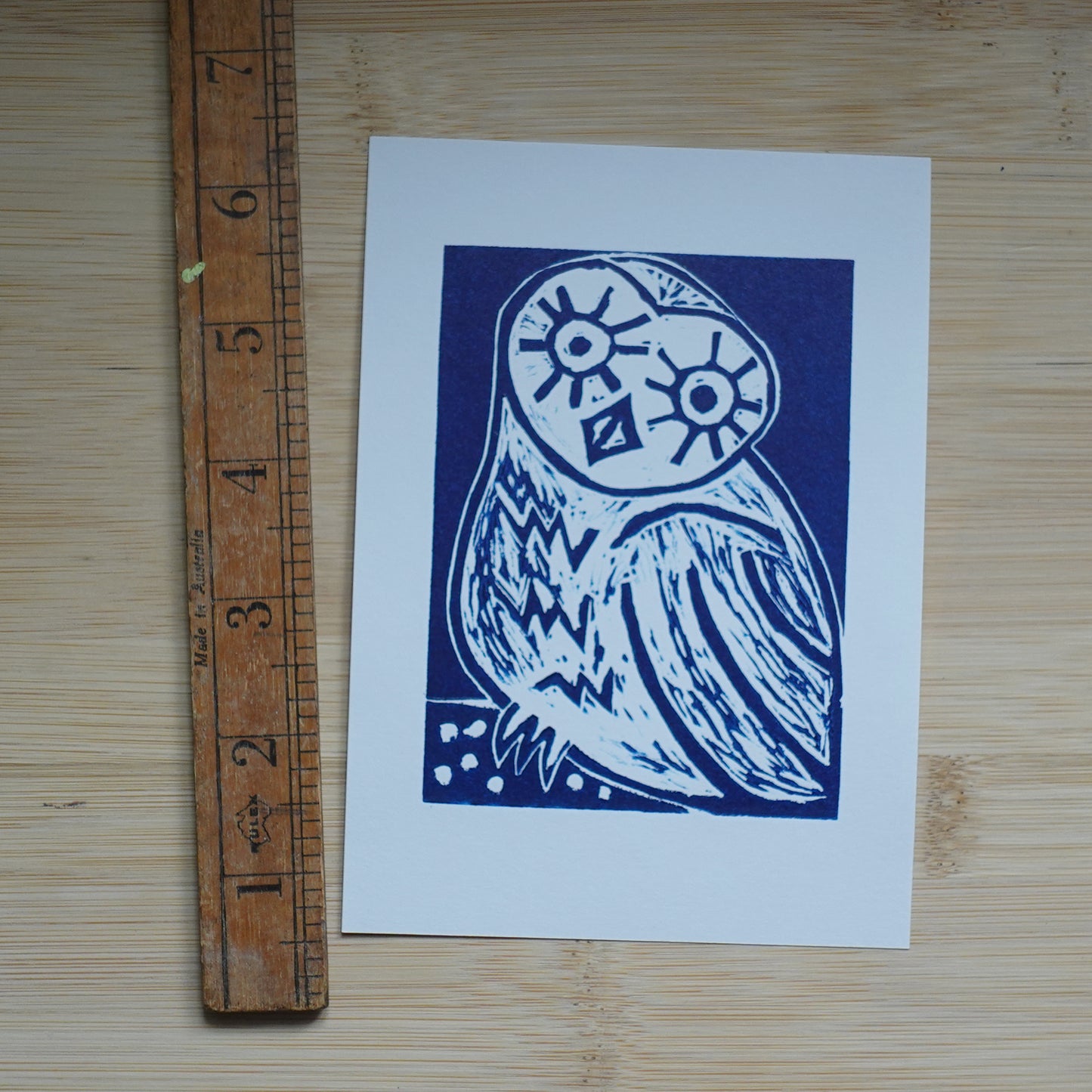 Blue Lino printed illustration of owl shown with wooden ruler for scale