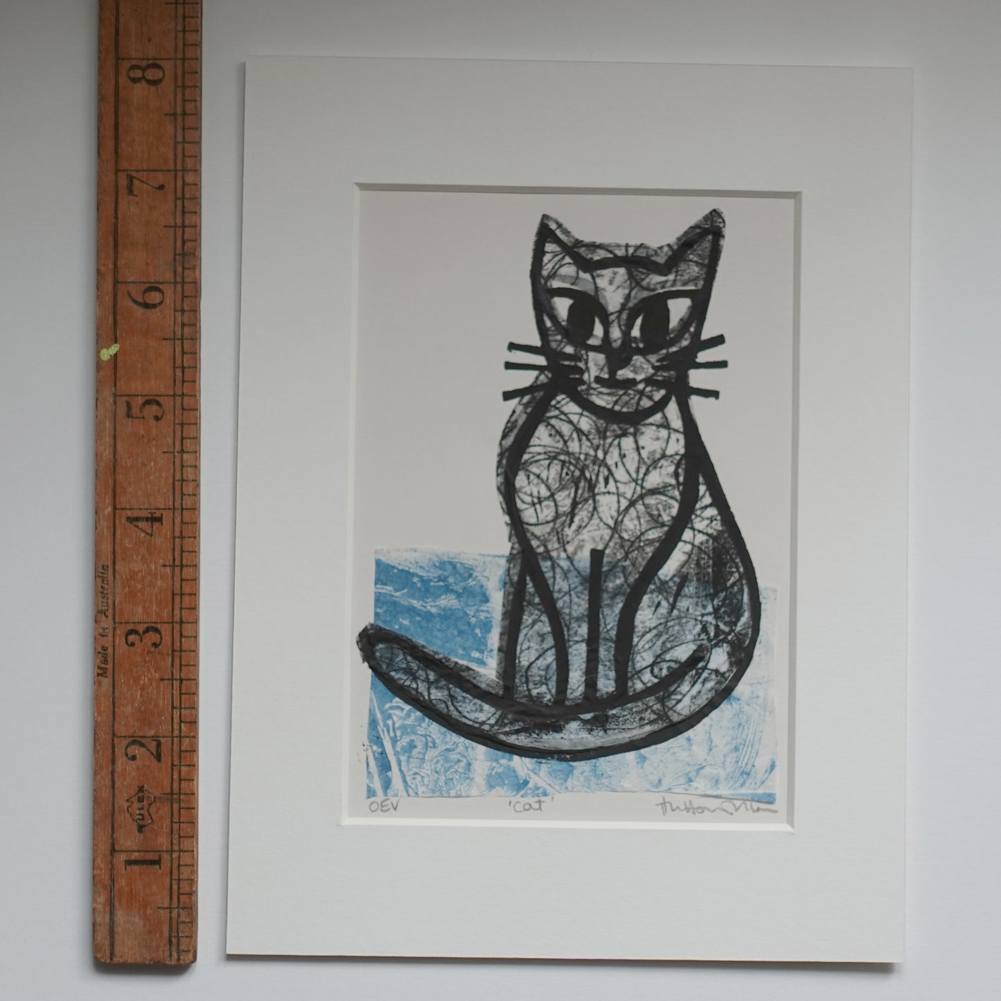 Lino print of cat, in black ink over chine-collé shown in mount with wooden ruler for scale