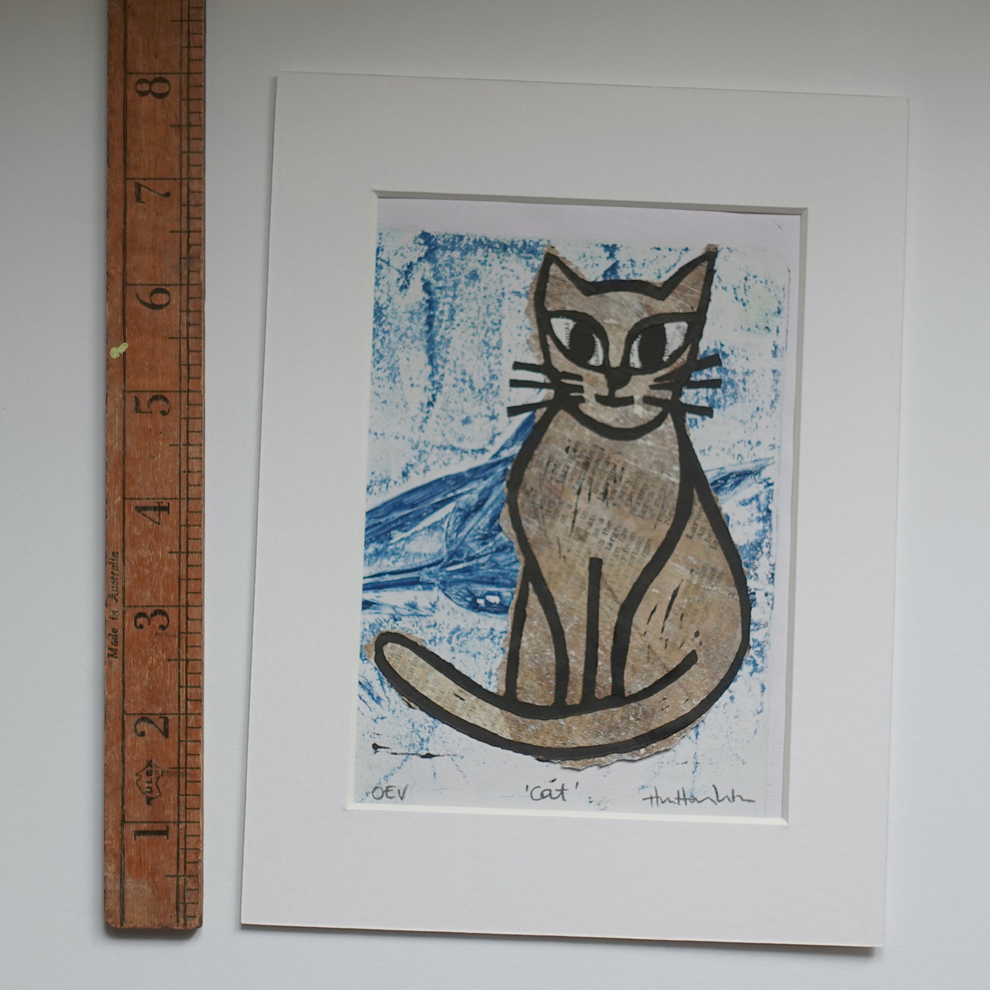 Lino print of cat, in black ink over chine-collé shown in mount with wooden ruler for scale