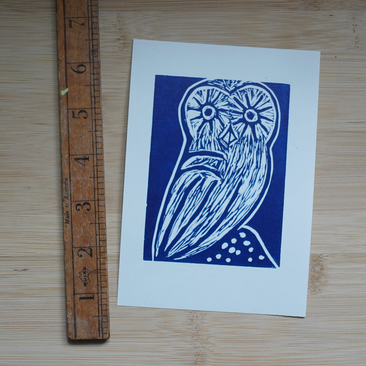 Blue Lino printed illustration of owl shown with wooden ruler for scale