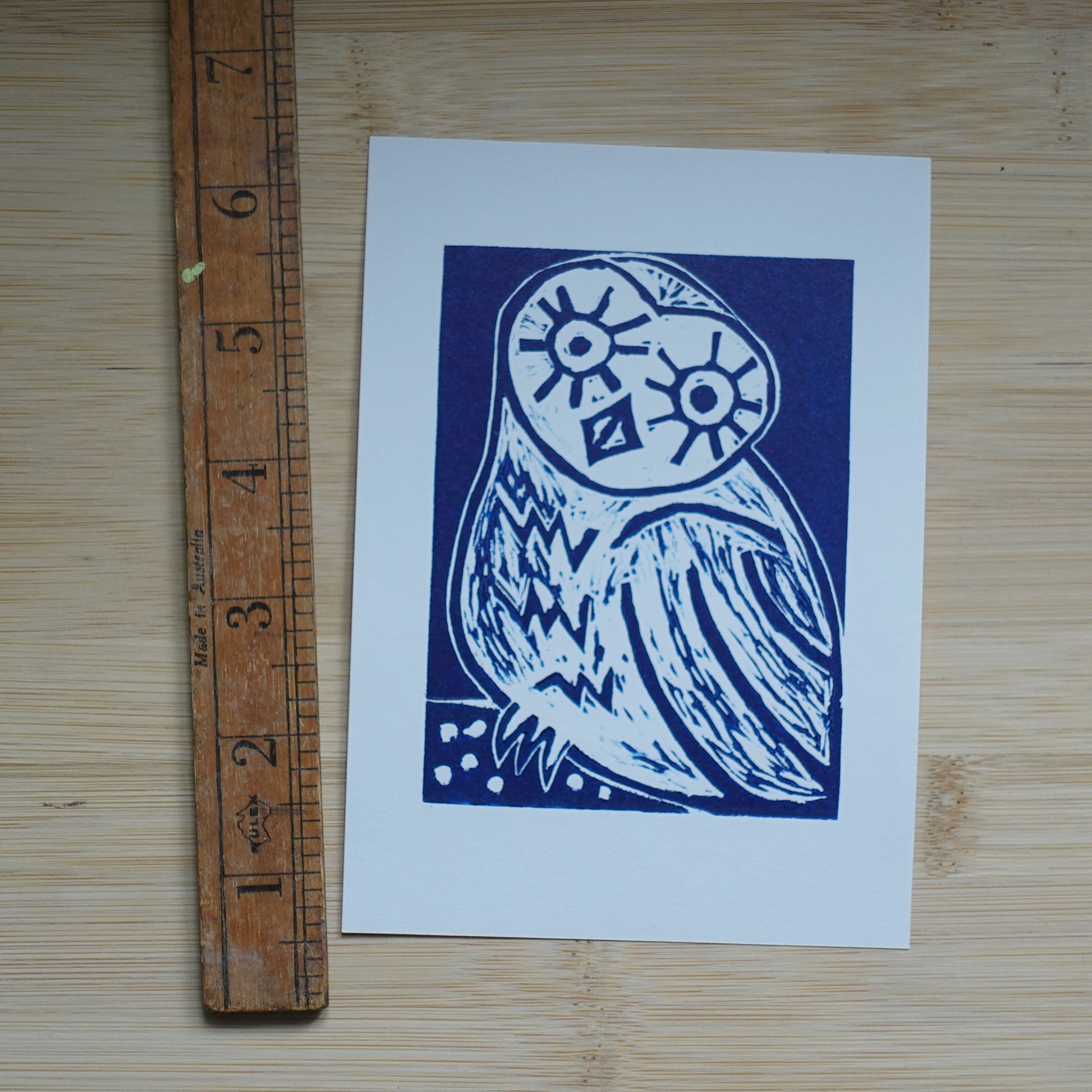 Blue Lino printed illustration of owl shown with wooden ruler for scale
