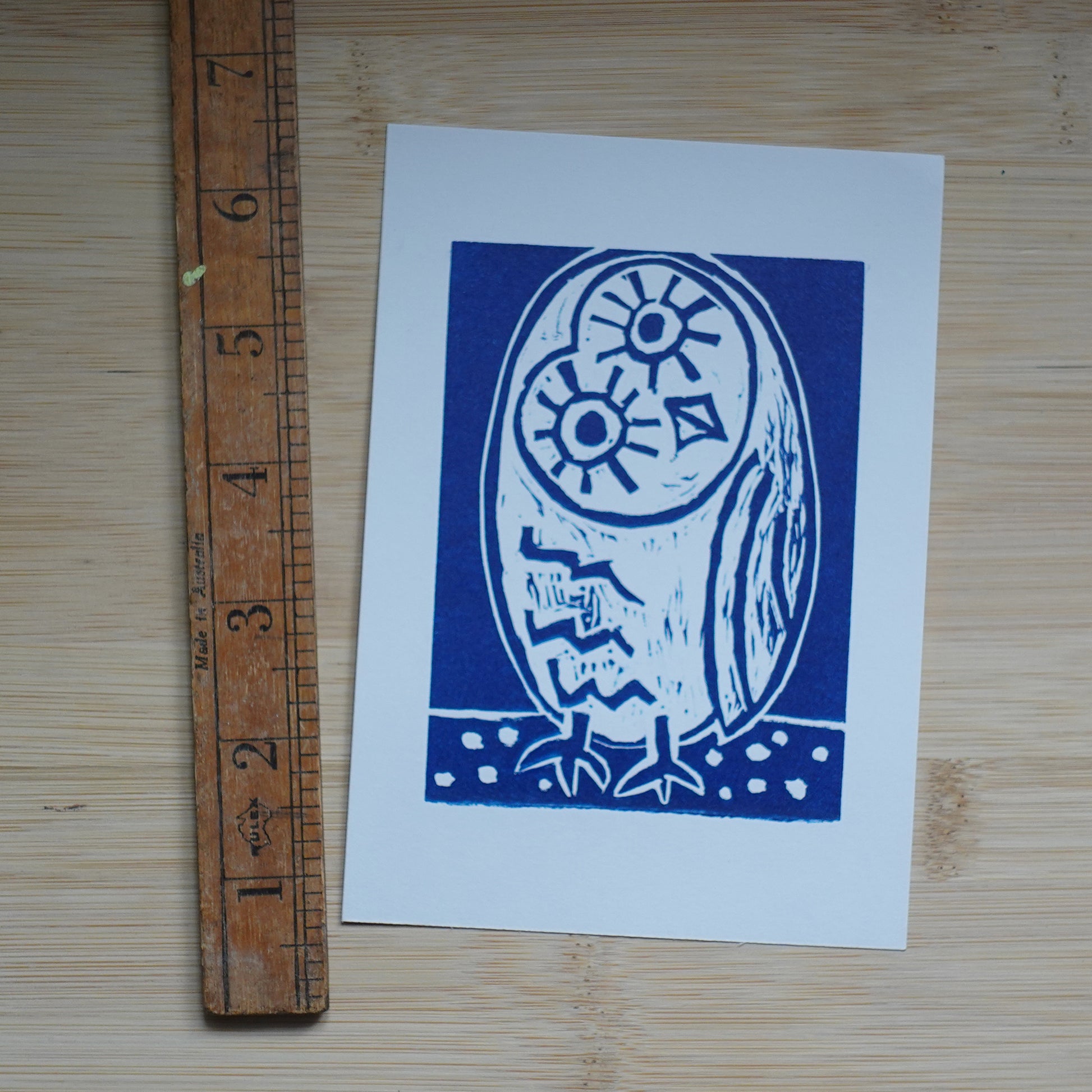 Blue Lino printed illustration of owl shown with ruler for scale