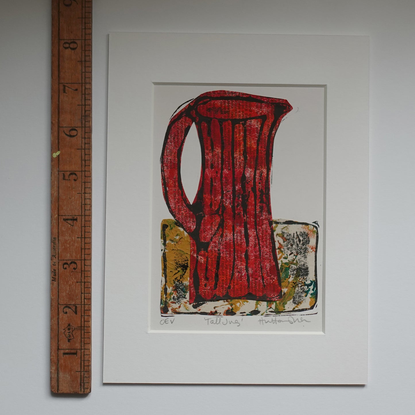 Relief print of tall jug, black ink over chine-collé shown in mount with wooden ruler for scale