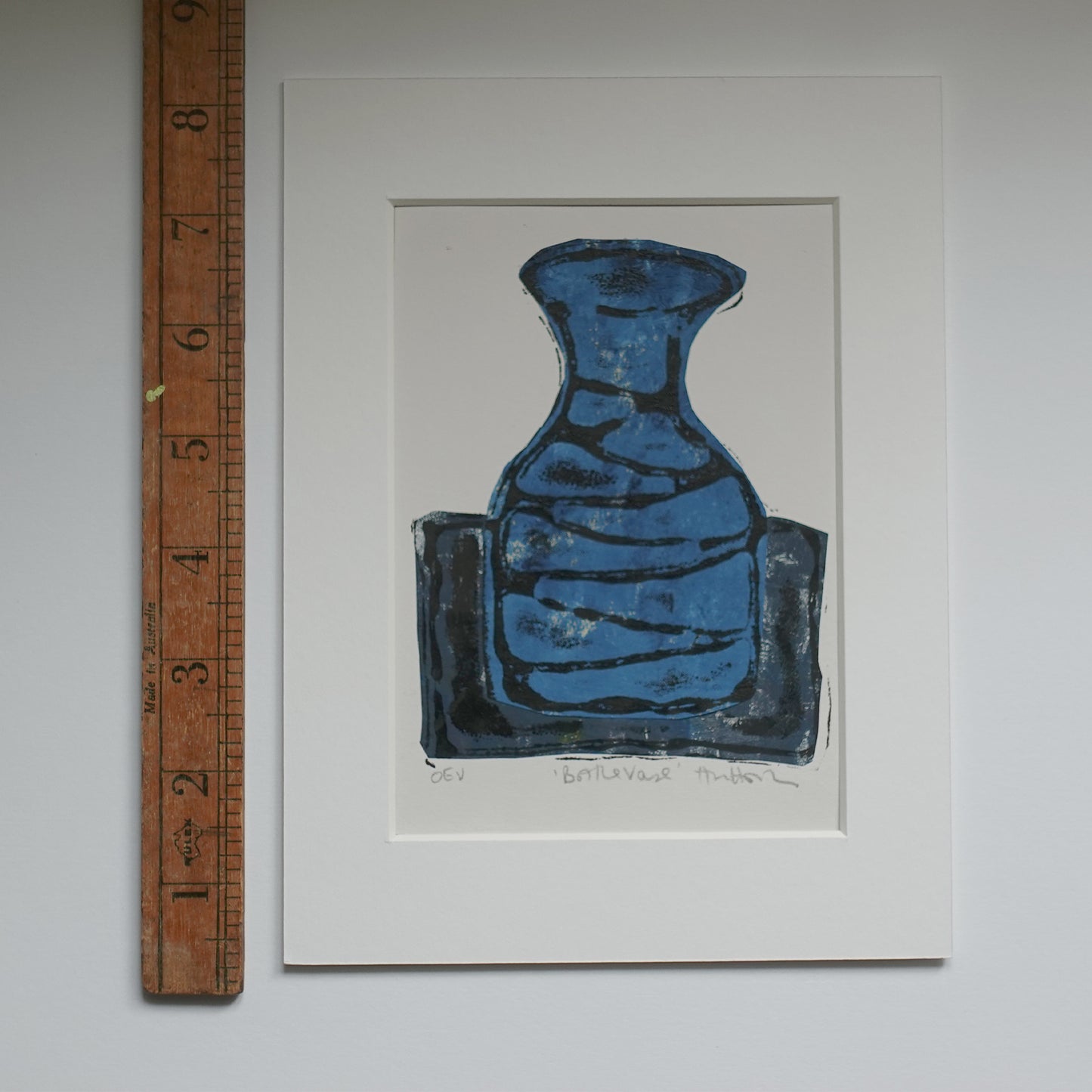 Relief print of bottle vase printed with black ink over chine-collé shown in mount with wooden ruler for scale