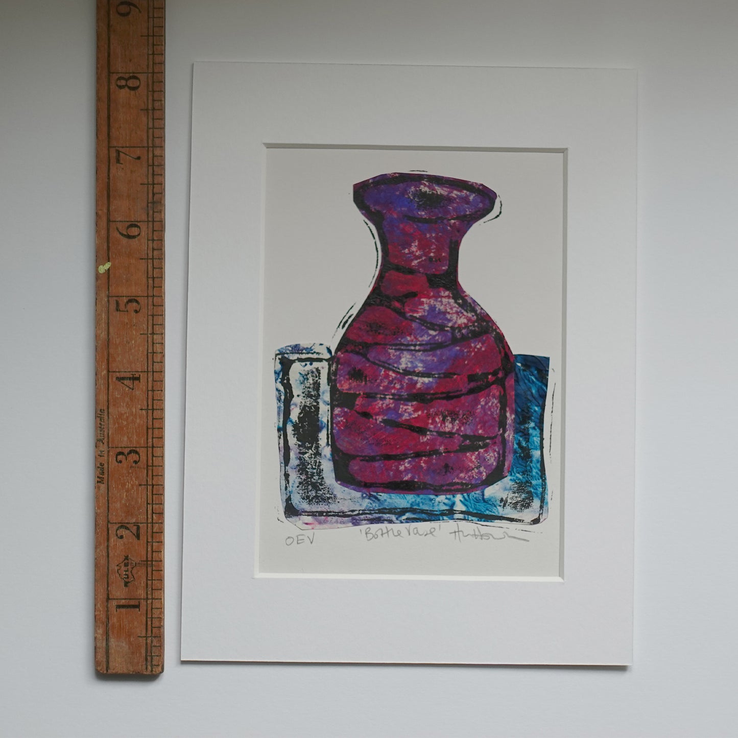 Relief print of bottle vase printed with black ink over chine-collé shown in mount with wooden ruler for scale